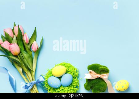 Easter composition tulips spring flowers eggs in a nest toy rabbit on a blue background. Stock Photo