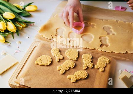 Female hand cutting pastry dough into bunnies shape while making sugar cookies. Close up. Easter backing concept. Home backing Stock Photo
