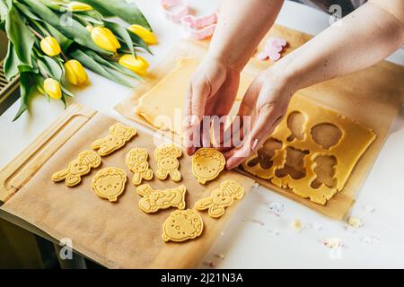 Female hand cutting pastry dough into bunnies and eggs shape while making sugar cookies. Close up. Easter backing concept. Home backing Stock Photo