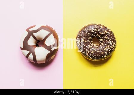 Two doughnuts with chocolate glaze on a pink and yellow background. Top view. Stock Photo