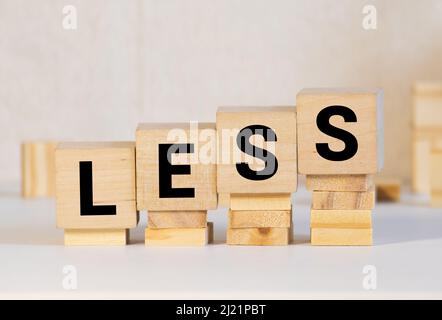 Less word on wooden cubic blocks with letters and stack of coins on it. Selective fofus. Spend less or cut costs business concept Stock Photo