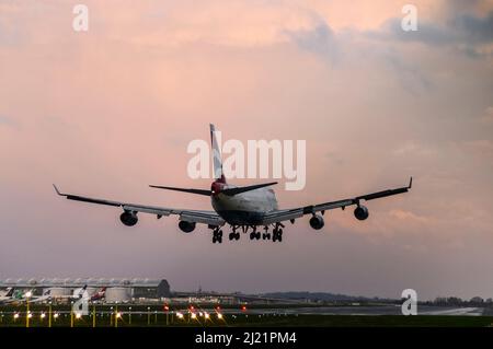 British Airways Boeing 747 -400 Jumbo Jet plane landing at London Heathrow Airport, UK, at dusk with sunset colours in cloudy sky. Runway lights Stock Photo