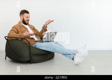 Freelancer Guy Video Calling Via Laptop Wearing Earbuds At Home Stock Photo