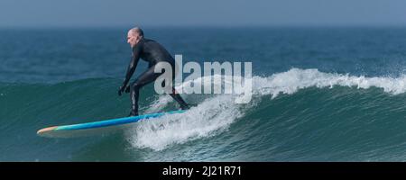 A panoramic image of a male surfer riding a wave at Fistral in Newquay in Cornwall in the UK. Stock Photo