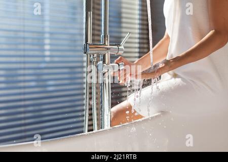Female Playing With Water Flowing From Tap While Sitting On Bathtub Edge Stock Photo
