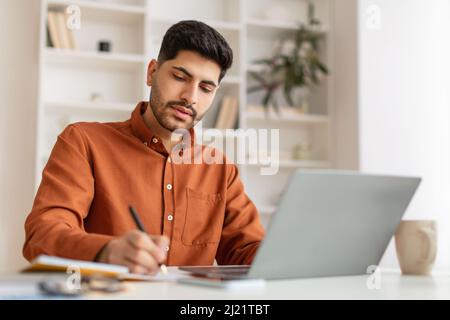 Portrait of focused Arab man using pc and writing Stock Photo
