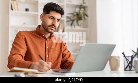 Portrait of focused Arab man using laptop and writing Stock Photo