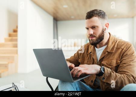 Serious Freelancer Man Using Laptop Computer Wearing Earbuds At Home Stock Photo