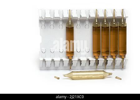Close up of one light brown open empty and several filled dark brown drinking ampoules in white cardboard stand behind on white background concept for Stock Photo