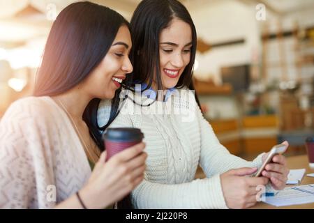 Check out this cute guy in my class. Shot of two young students using a smartphone while studying together in a cafe. Stock Photo