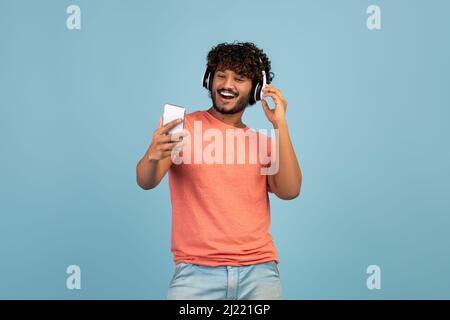 Excited eastern guy using wireless headset and smartphone, copy space Stock Photo