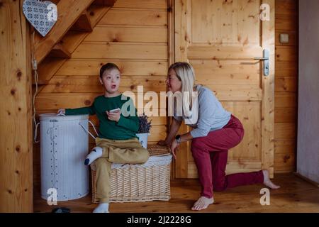 Child with Down syndrome sitting on floor and using tablet with grandmother at home. Stock Photo