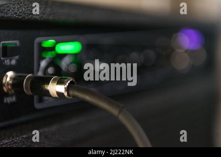 Cable from a bass connected to the amp where you can see some lights and knobs to control the sound. Stock Photo