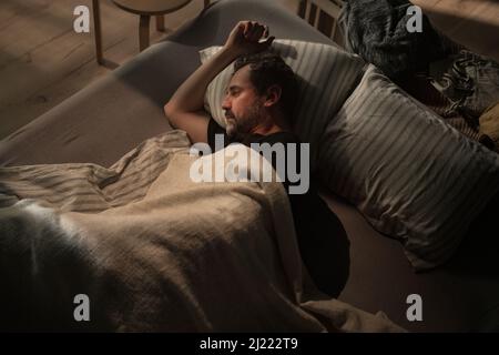 Sad mature man suffering from covid depression lying in bed in night. Stock Photo