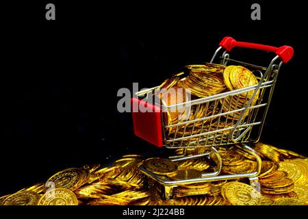 Golden coin in the shopping cart on a stacking gold coins at black background Stock Photo