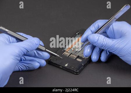 Process of mobile phone repair. Hands of a service worker repairing modern mobile phone. Stock Photo