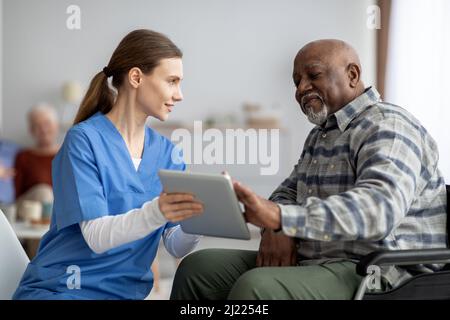 Friendly nurse helping black senior man using digital tablet Stock Photo