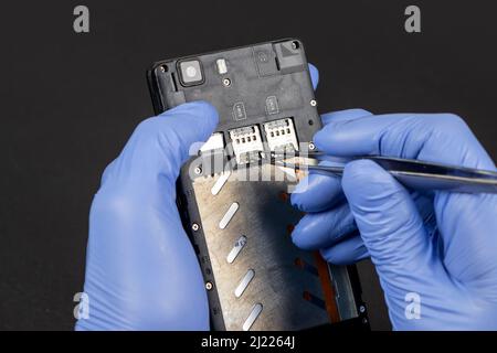 Process of mobile phone repair. Hands of a service worker repairing modern mobile phone. Stock Photo