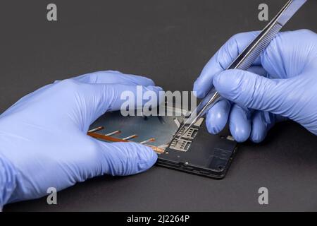 Process of mobile phone repair. Hands of a service worker repairing modern mobile phone. Stock Photo