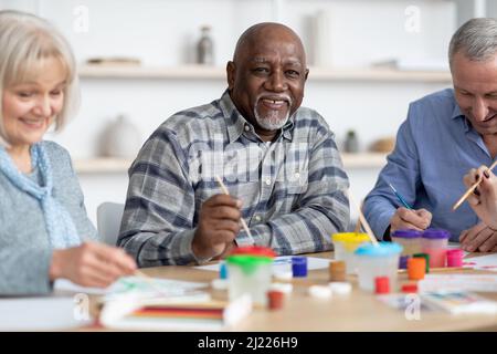 Happy senior black man enjoying painting activity with his friends Stock Photo