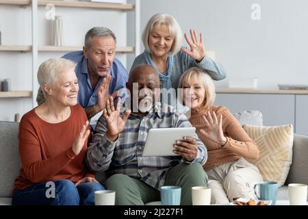 Positive multiracial senior friends having video conference, using pad Stock Photo