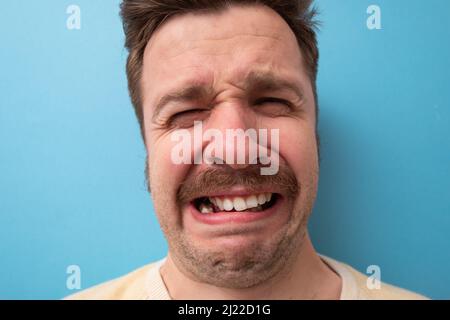 Funny caucasian man crying wipes tears losing his job. Studio shot on blue background. Stock Photo