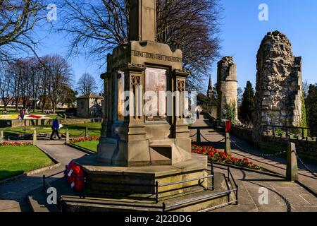 People relaxing walking on paths in sunny park (war memorial red poppies, ancient ruins, blue sky) - Knaresborough Castle, North Yorkshire England UK. Stock Photo