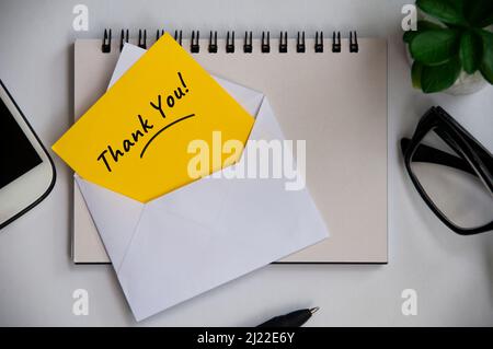 Thank you note on yellow paper in an envelope with office background concept. Appreciation concept Stock Photo