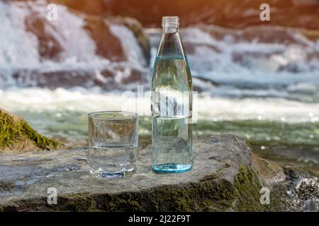 Natural drinking water in a bottle and glass beaker on nature background river. Stock Photo