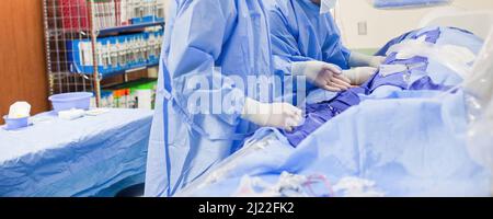 Two non-descript surgeon doctors doing a surgery in a surgical room wearing operating blue scrubs and white latex gloves Stock Photo