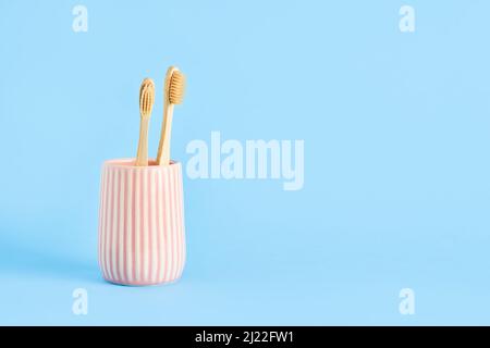 Two bamboo toothbrushes in a pink ceramic holder on a blue background. Eco-friendly, zero-waste concept. Copy space for text, selective focus Stock Photo