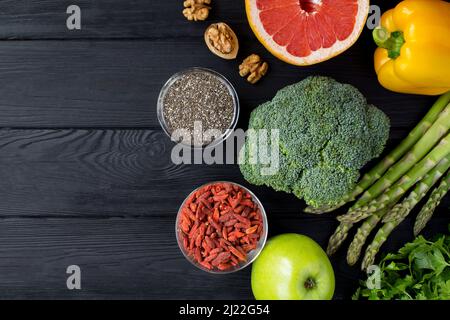 Vegetable, fruit, chia seeds and goji berry on the black wooden background. Top view. Copy space. Stock Photo