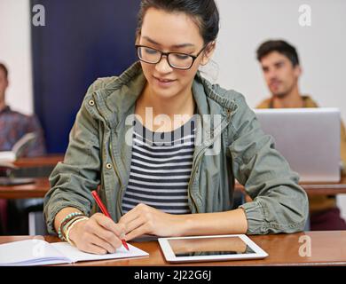 Doing the work to achieve her dreams. Cropped shot of a young woman using notes and digital tablet in class. Stock Photo