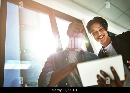 Check out these cool features. Shot of two young colleagues looking at a tablet together in the office. Stock Photo