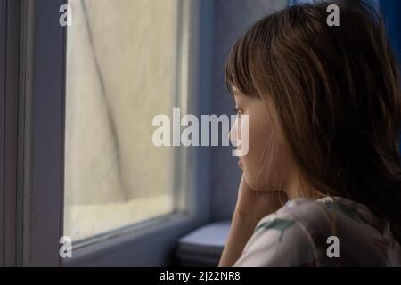 Little sad girl near window. Abuse of children concept Stock Photo