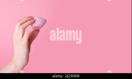 Banner with hand holding makeup sponge or blender on pink background. Beauty concept. Applying foundation, concealer, balms. Face contouring. Copy space. High quality photo Stock Photo