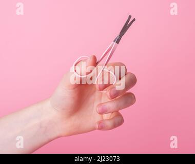 Woman hand holding nail scissors for manicure on pink background. Tool for beauty procedure. Hygiene and care concept. High quality photo Stock Photo