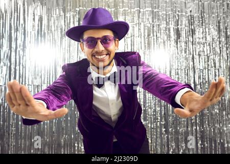 Happy funny smiling man wearing purple jacket, hat and glasses having fun at party Stock Photo
