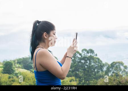 young latina woman taking a picture of a landscape in the beautiful colombian mountains. influencer girl creating content for her social networks, whi Stock Photo