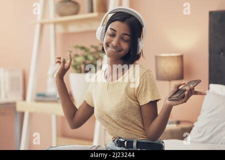 Good music gets your mind off everything else. Shot of a young woman using headphones in her bedroom at home. Stock Photo