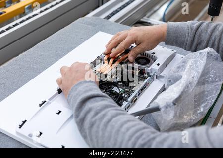 Photo of hands of man who assembles a computer monitor system block on an conveyor belt at a monoblock assembly plant. Engineer works on a modern high Stock Photo