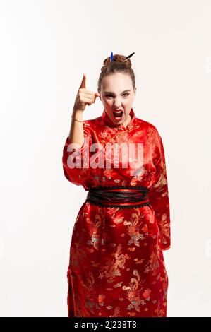 young man in red oriental costume, looking directly at the camera, shouting and raising his arm in a threatening and reprimanding gesture with his fin Stock Photo