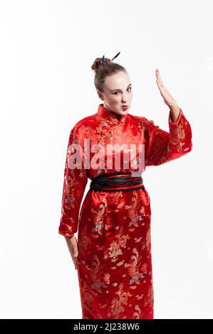 young man in a red oriental suit, looking at the camera and wrinkling his nose and raising his arm in reprimand against a white background Stock Photo