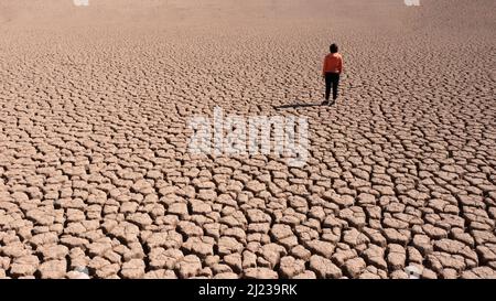 Silhouette of a man on a sandy cracked empty not fertile land during a drought. The concept of ecological catastrophe on the planet. Stock Photo