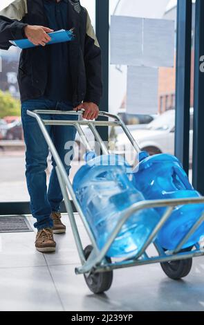 Bottled and delivered straight to your door. Cropped shot of a courier making a bottled water delivery in an office. Stock Photo