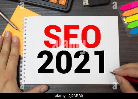 seo 2021, text on white notepad near keyboard, blue pencils, black magnifier. on white background. Stock Photo