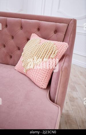 Knitted handmade pillow with pink threads lies on the sofa. Stock Photo