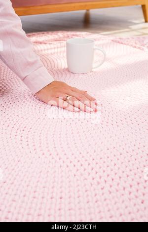 Women's hands lie on a plaid of coarse knitted wool on a wooden floor, top view. Handmade carpet Stock Photo