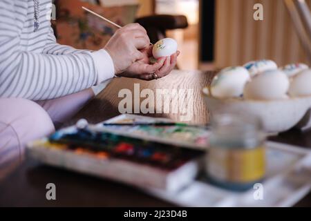 Process of woman paiting a water colors on fantasy chicken eggs. Female preparing for Easter egg festival Stock Photo