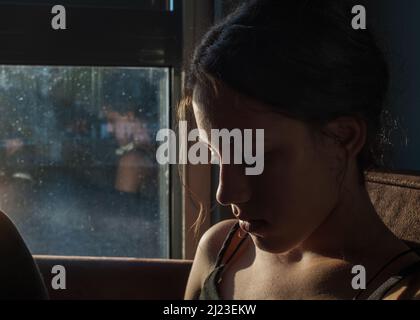 A young woman sits on a sofa near window sunlight on her face Stock Photo